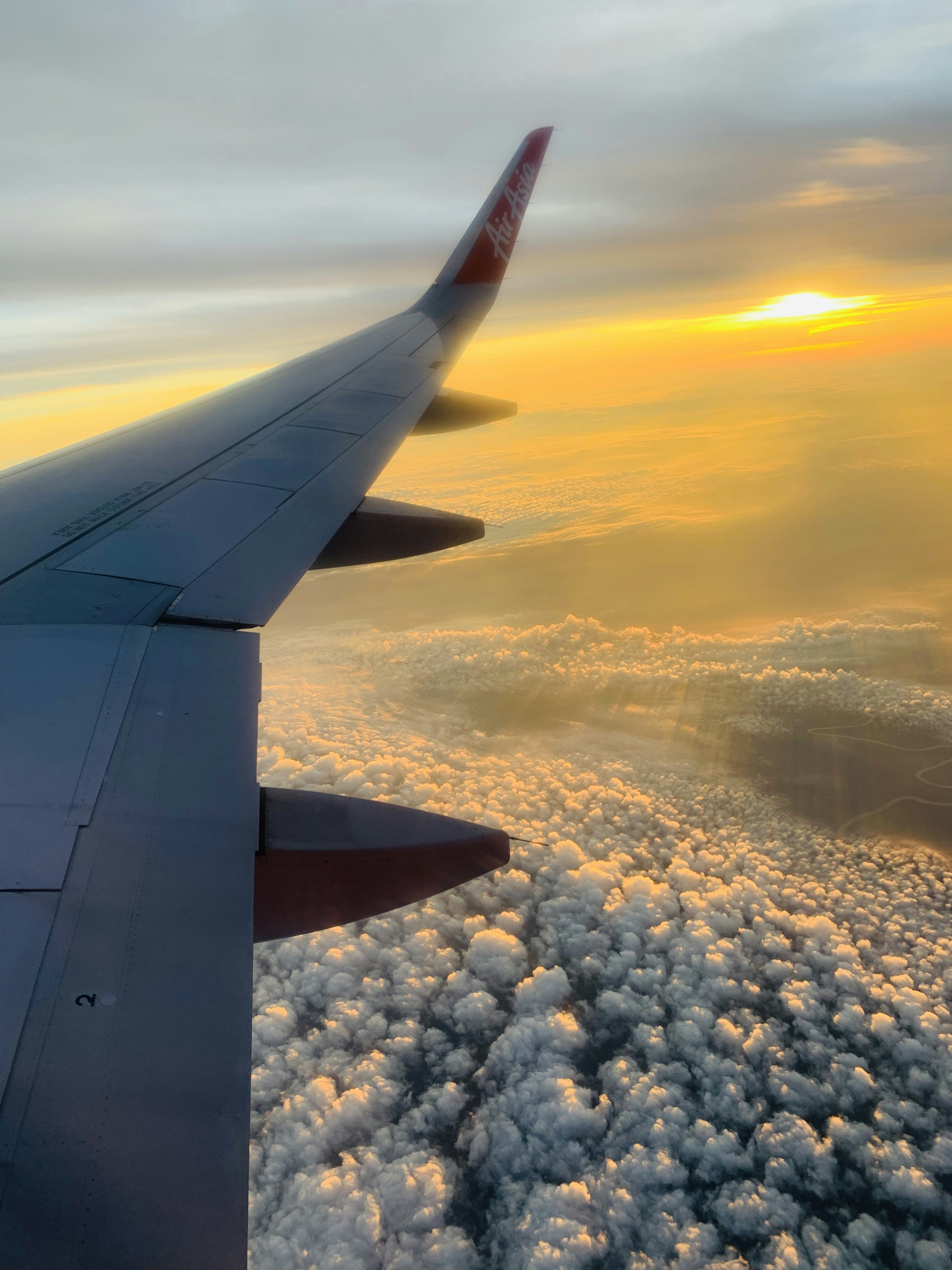 Airplane flying above clouds at sunrise with warm golden light, aerial view from above
