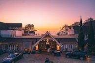 Evening shot of a villa with warm lights glowing through large windows, framed by tall trees.