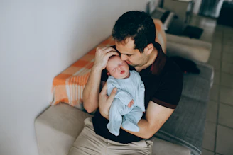man in black crew neck t-shirt carrying baby in blue and white stripe onesie