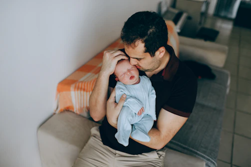 man in black crew neck t-shirt carrying baby in blue and white stripe onesie