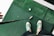 A person wearing green and white sneakers stands on green artificial turf, holding a golf club near a golf ball.