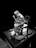 A sculpture of a person seated on a wooden chair with hands clasped in a posture of contemplation or prayer. The figure is draped in a hooded robe, with intricate detailing on the chair and base. The setting appears dramatic, with a strong contrast against the dark background.