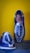 Two handmade, woven leather sandals are displayed against a vibrant yellow wall. The shoes feature a striking blue and white pattern with intricate weaving, showcasing craftsmanship and attention to detail.