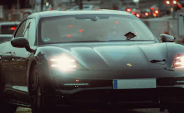 Urban night driving scene featuring a modern car with glowing headlights cutting through the city streets.