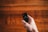A hand holding a remote control against a wooden surface. The remote has various buttons, some of which include a microphone and power button, and there is a warm, soft focus background.