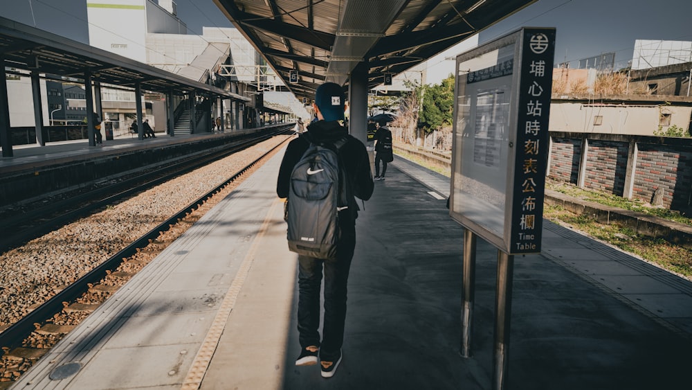 man in black jacket and blue denim jeans standing on train station during daytime