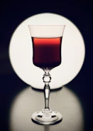 Close-up of a hand pouring deep red wine into a crystal glass against a softly lit backdrop.