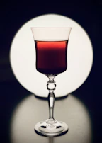 Elegant photo of a wine glass filled with red wine, softly lit against a dark background.