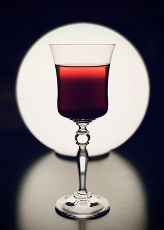 Elegant close-up of a wine glass catching soft light, set against a deep green background.