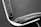 A close-up of a modern chair featuring black leather upholstery with visible stitches and a metallic frame. The image highlights the sleek lines and minimalist design of the chair against a plain background.