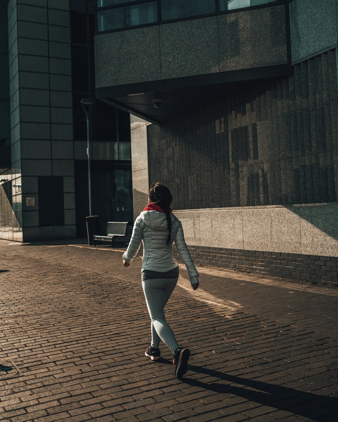 woman in gray jacket and gray pants walking on brown brick floor during daytime