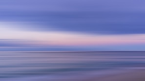 A serene, abstract image featuring smooth horizontal lines in shades of blue and pink, evoking a calming seascape or sky transition.