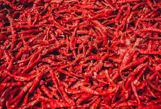 A close-up view of a large pile of dried red chili peppers. The peppers are arranged in a dense, overlapping fashion, showcasing their wrinkled texture and vibrant red color.