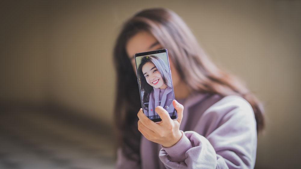 donna in camicia bianca a maniche lunghe che tiene uno smartphone nero