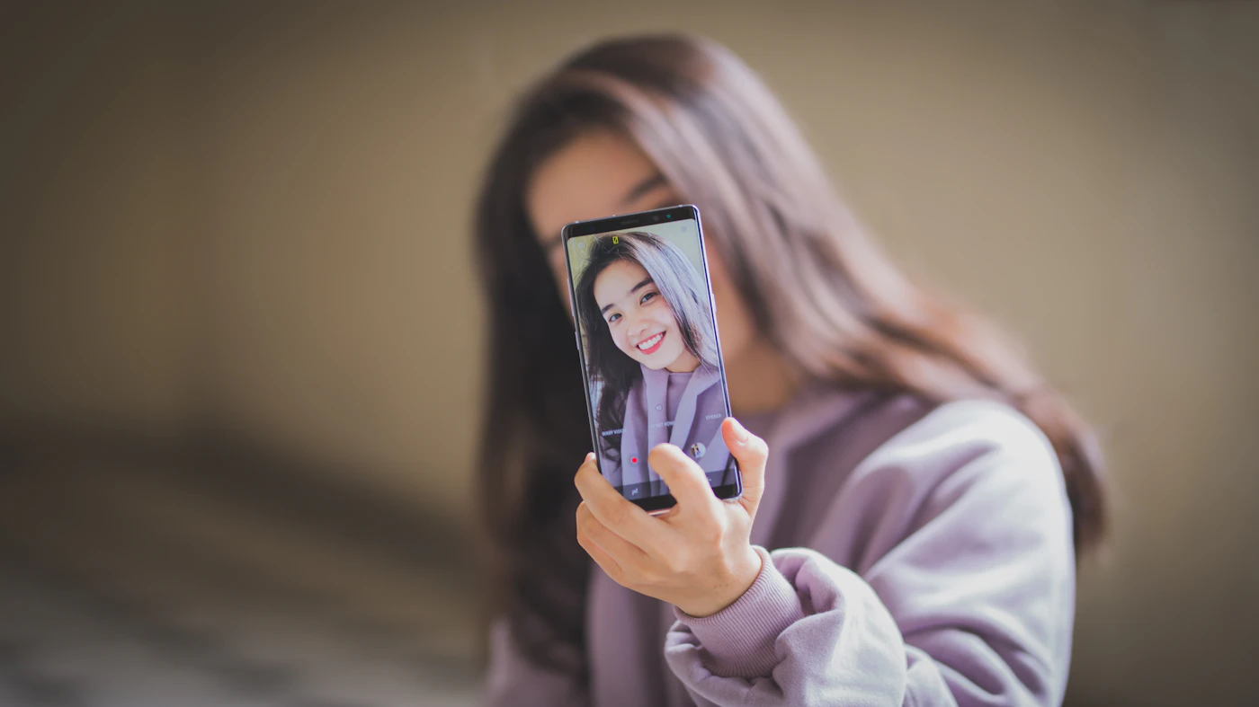 A woman holds up a smartphone whose screen shows her face through the front camera