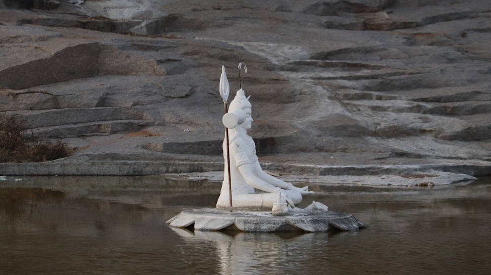 A serene close-up of Lord Shiva's trident resting against a backdrop of flowing river water at dawn.