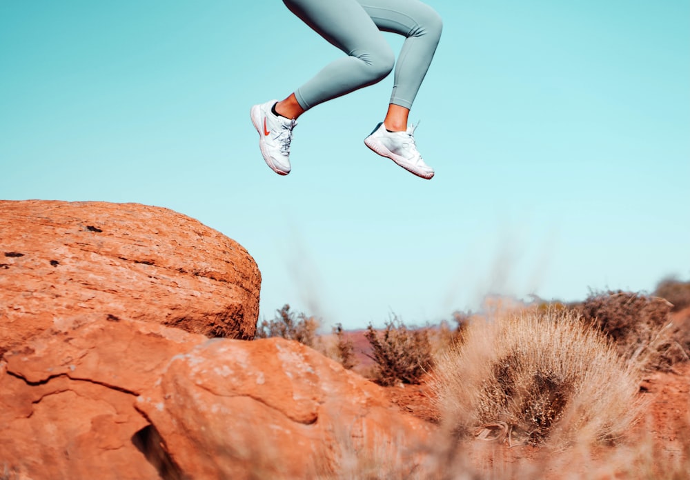 woman in blue denim jeans and white sneakers sitting on brown rock during daytime