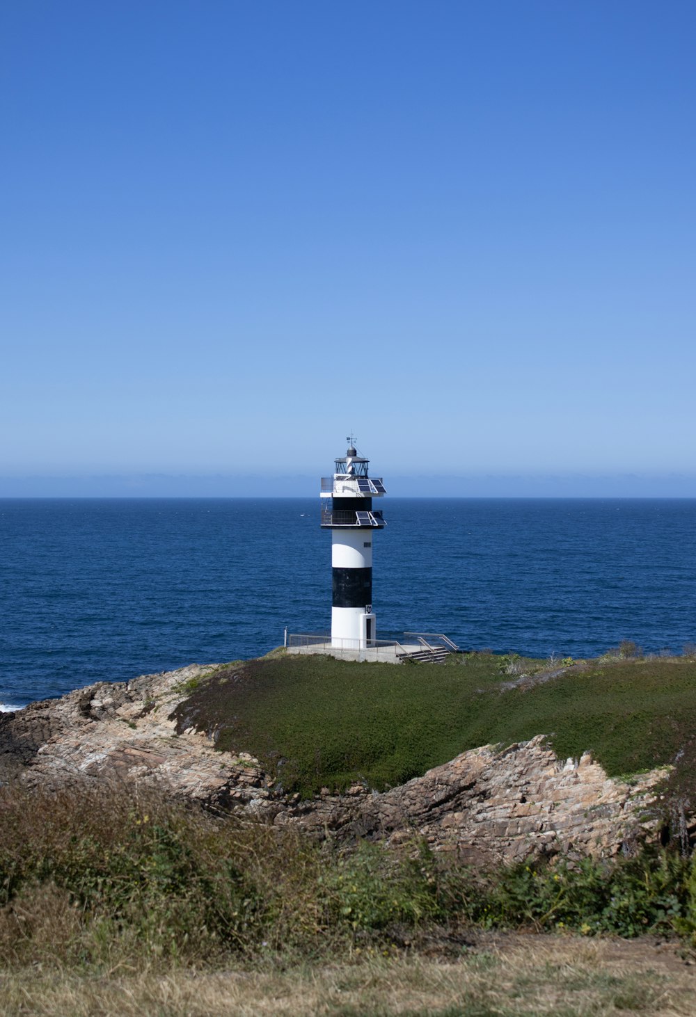 white and black lighthouse on green grass field near blue sea under blue sky during daytime