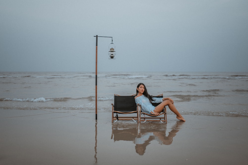 woman in white tank top sitting on black and gray chair on beach during daytime