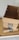 Three cardboard boxes with Amazon Prime branding are stacked on top of a wooden surface. The top box is open, revealing its interior. A light gray wall serves as the background.
