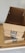 Three cardboard boxes with Amazon Prime branding are stacked on top of a wooden surface. The top box is open, revealing its interior. A light gray wall serves as the background.