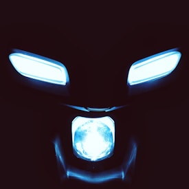 Bright blue lights are arranged in a way that resembles a stylized or abstract face, set against a dark background. Two elongated, oval-shaped lights are positioned at the top, with a larger round light at the bottom, giving the impression of eyes and a mouth.
