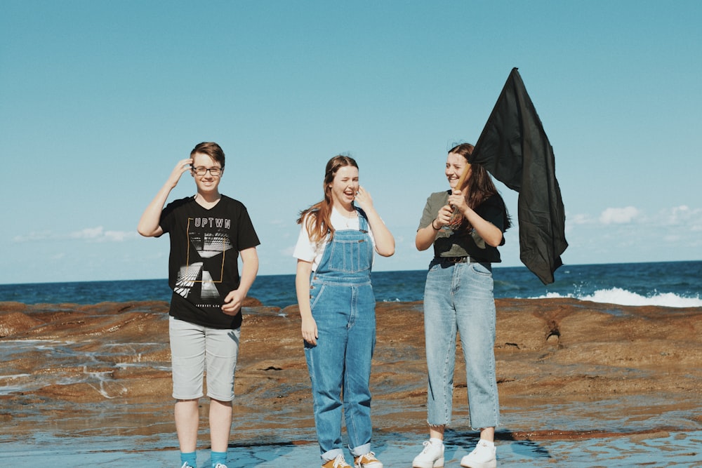 3 women standing on brown rock near body of water during daytime