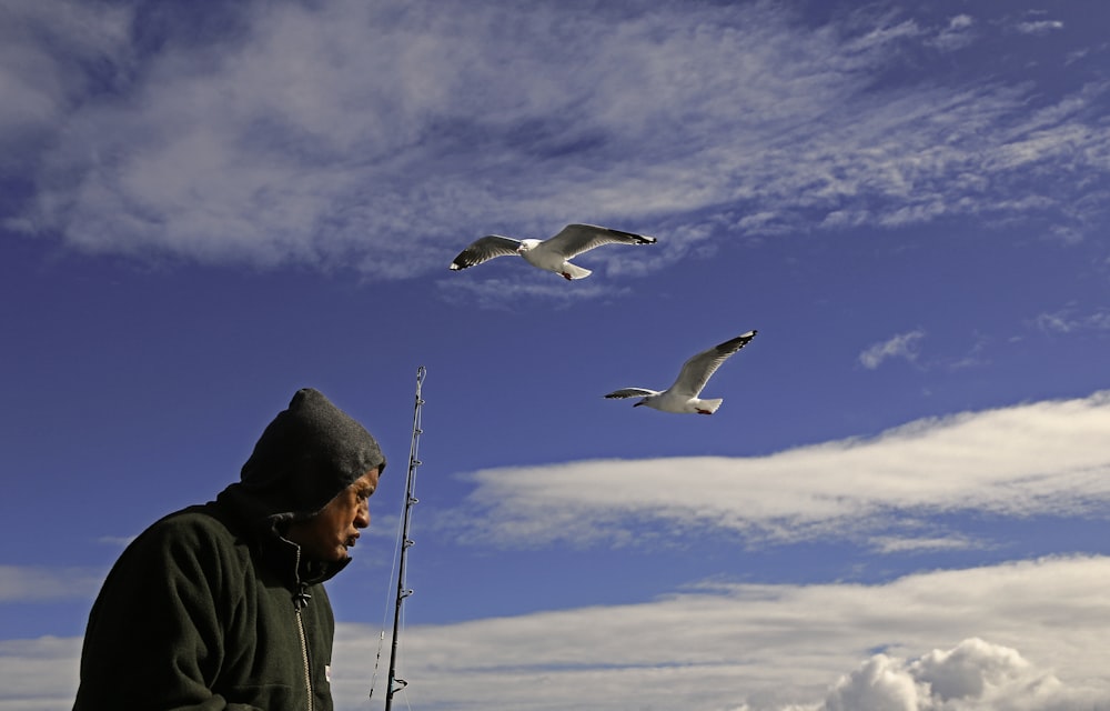 man in black jacket and black cap standing on black rope with white bird flying during