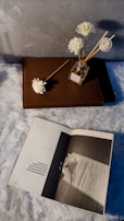 An open book with notes and sketches about fragrance making, surrounded by raw materials.