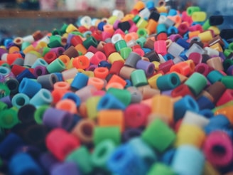 A vibrant and colorful assortment of small, cylindrical plastic beads. They are densely packed and come in a wide variety of colors, including red, blue, green, yellow, pink, and orange. The beads create a lively and textured visual display.