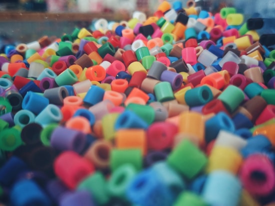 A vibrant and colorful assortment of small, cylindrical plastic beads. They are densely packed and come in a wide variety of colors, including red, blue, green, yellow, pink, and orange. The beads create a lively and textured visual display.