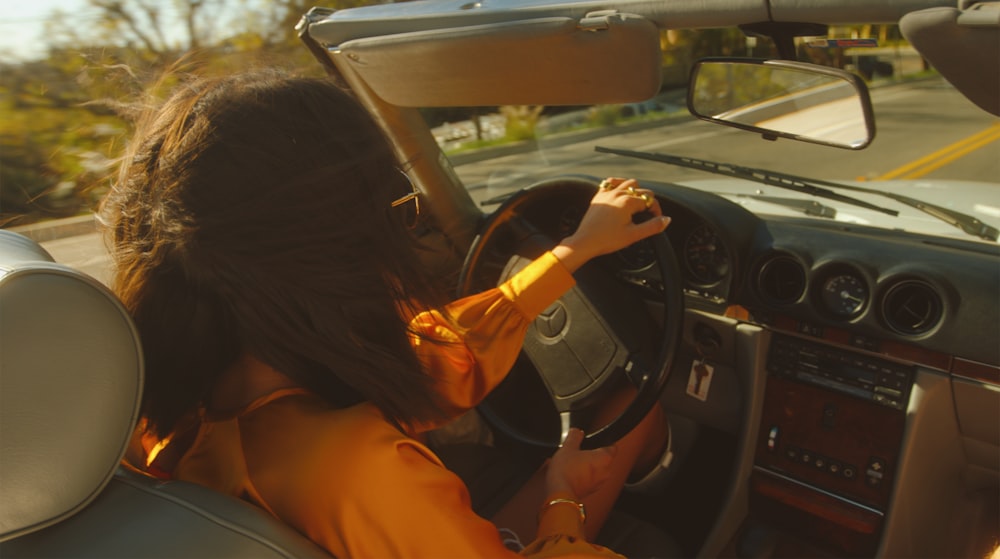 オレンジ色のシャツを着た女性が車を運転する
