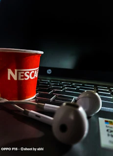 Earphones placed beside a laptop and a cup of coffee on a cozy desk setup