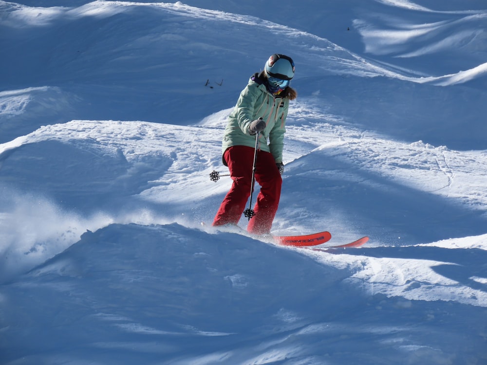 man in green jacket and blue pants riding red snowboard on snow covered mountain during daytime