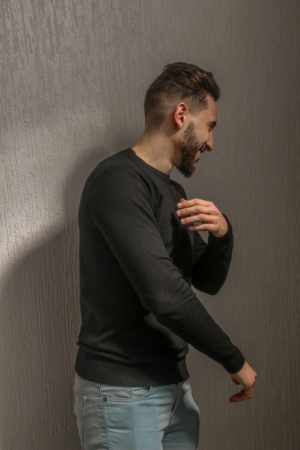 homme en chemise à manches longues noire debout à côté d’un mur blanc