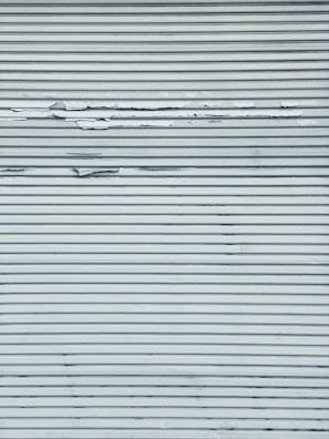 A metal surface featuring horizontal lines with visible peeling and chipping paint, creating a textured appearance.