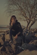 woman in black jacket sitting on rock