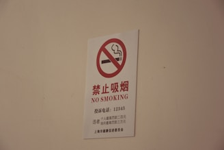 A white sign with a red circle and diagonal line crossing out a smoking cigarette icon, accompanied by text in both Chinese characters and English that reads 'NO SMOKING'.