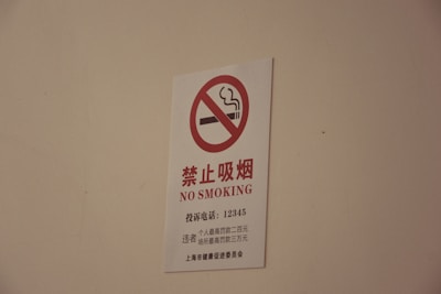 A white sign with a red circle and diagonal line crossing out a smoking cigarette icon, accompanied by text in both Chinese characters and English that reads 'NO SMOKING'.