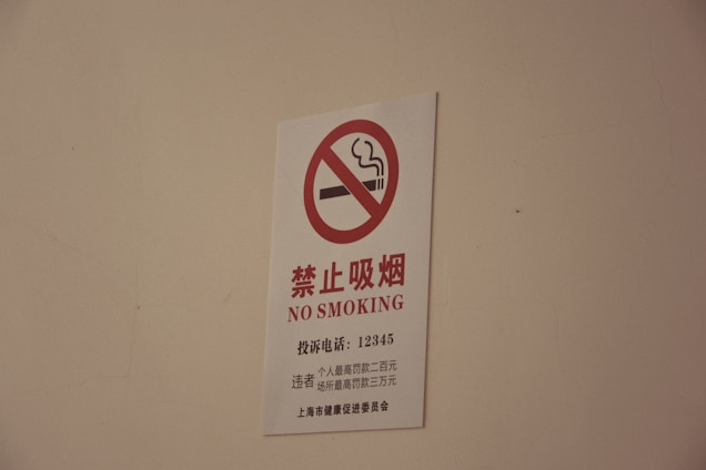 A white sign with a red circle and diagonal line crossing out a smoking cigarette icon, accompanied by text in both Chinese characters and English that reads 'NO SMOKING'.