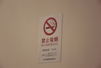 A white sign with a red circle and diagonal line crossing out a smoking cigarette icon, accompanied by text in both Chinese characters and English that reads 'NO SMOKING'.