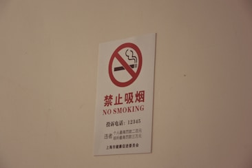 A white sign with a red circle and diagonal line crossing out a smoking cigarette icon, accompanied by text in both Chinese characters and English that reads 'NO SMOKING'.