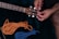 A person is adjusting the tuning pegs on a guitar headstock. Next to the guitar, there are two pieces of rope: one orange and one blue, neatly coiled on a dark surface.