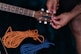 A person is adjusting the tuning pegs on a guitar headstock. Next to the guitar, there are two pieces of rope: one orange and one blue, neatly coiled on a dark surface.