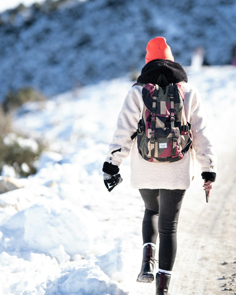 Frau in weißer Jacke und schwarzer Hose geht tagsüber auf schneebedecktem Boden spazieren