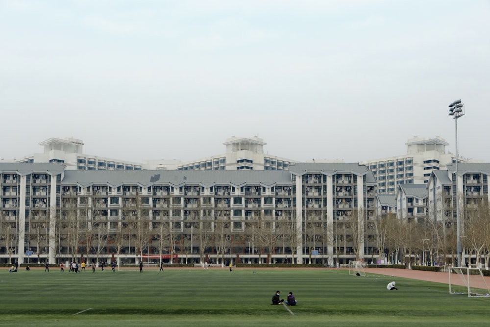 Persone che camminano sul campo di erba verde vicino all'edificio in cemento bianco durante il giorno