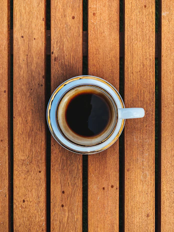 A steaming cup of rich, dark coffee served on a minimalist wooden table.