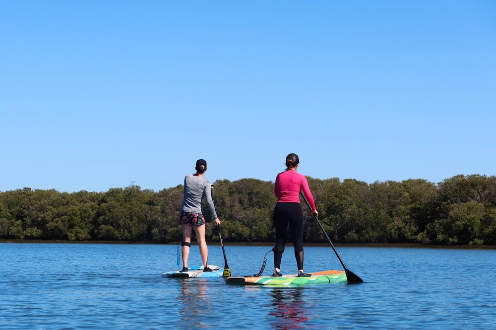 man in gray shirt and blue shorts standing on yellow kayak on body of water during