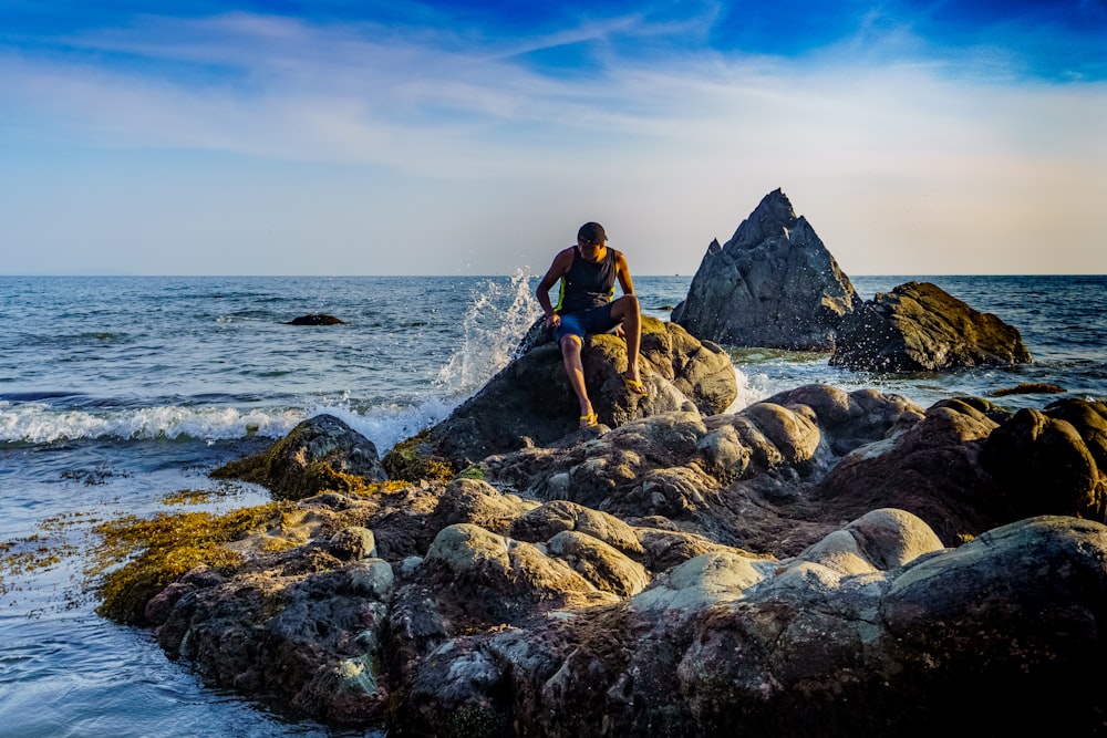 man in black t-shirt and black shorts standing on rocky shore during daytime