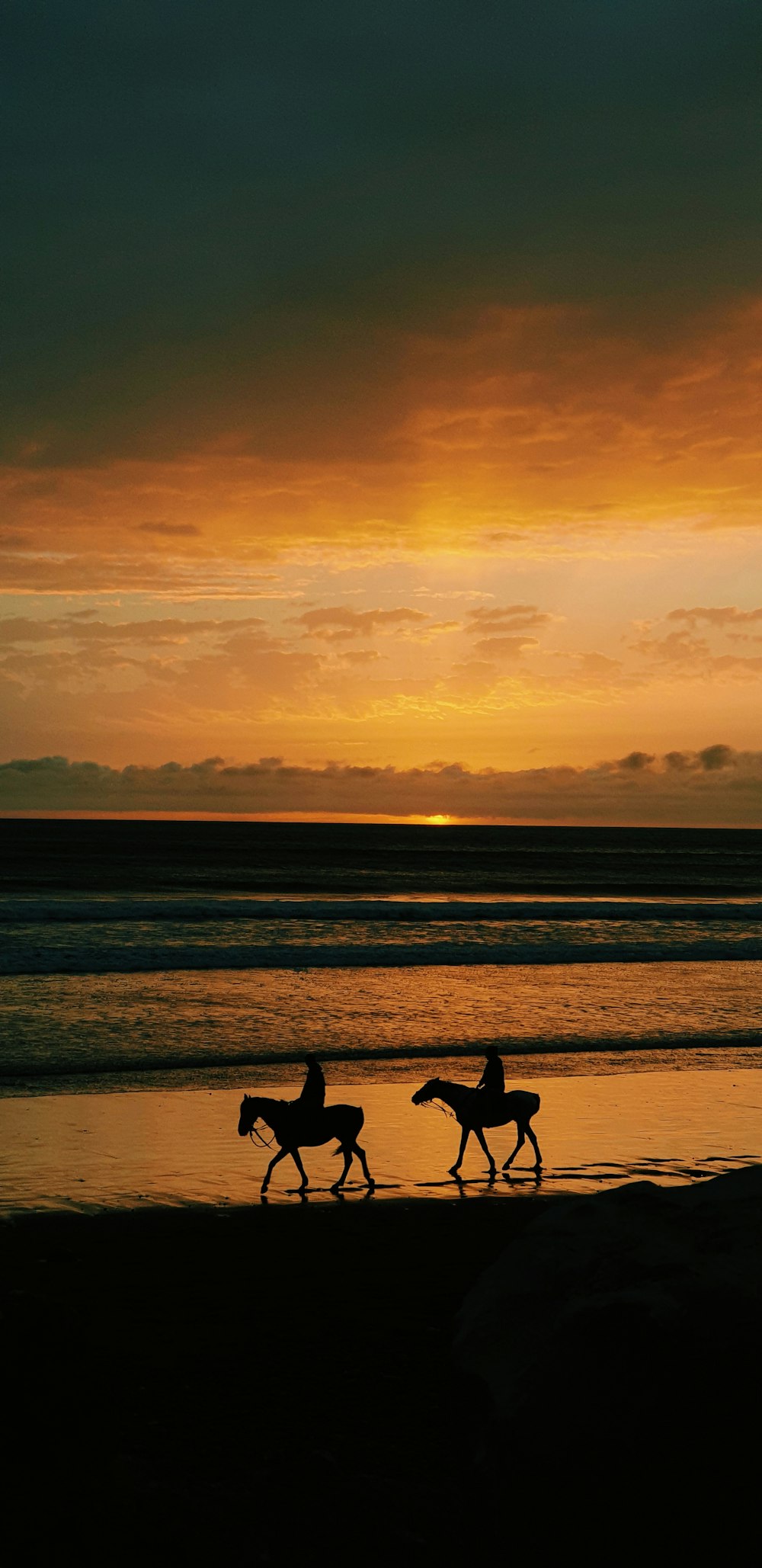 Silhouette von 2 Personen, die während des Sonnenuntergangs am Strand spazieren gehen